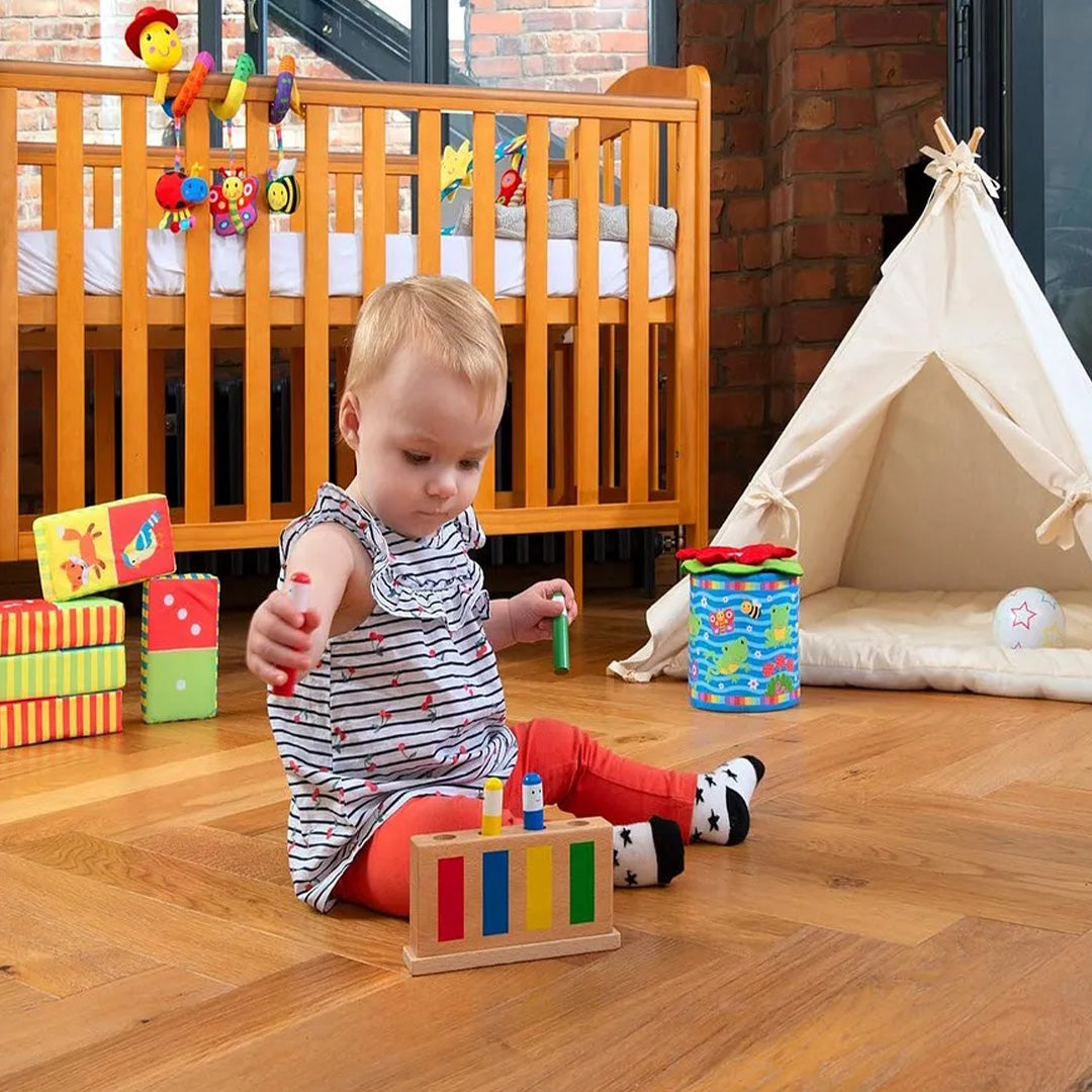 A toddler's hand pressing one of the colourful figures to make it bob up

